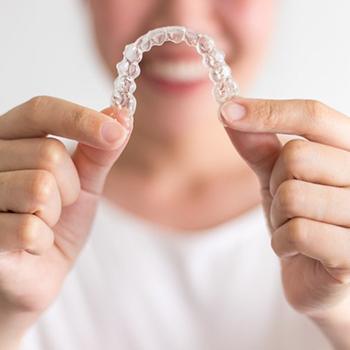 Smiling woman holds Invisalign in Hampton in front of her