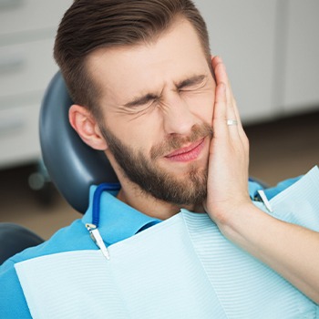 Man in dental chair holding cheek