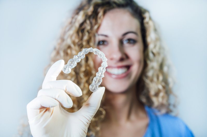 a woman wearing a glove and holding an Invisalign aligner in her right hand