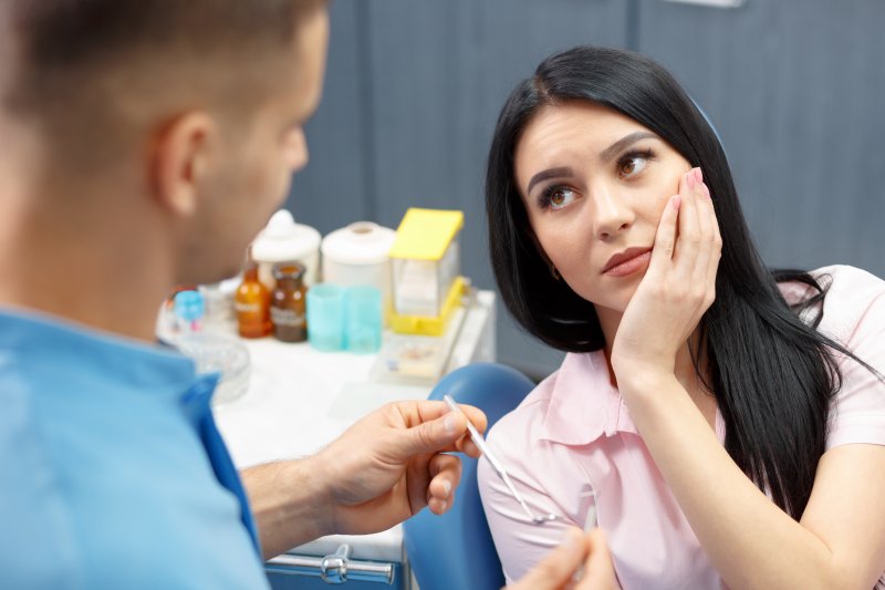 Woman holding cheek while sitting in dental chair at her dentist