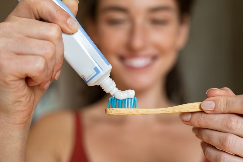 A woman applying toothpaste to a bamboo toothbrush
